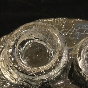 May include: A clear glass candle holder with three circular depressions for candles. The glass has a textured surface.