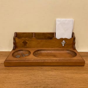 May include: A brown wooden desk organizer featuring a back section with three compartments, one holding white paper, and a front section with a circular tray containing metal paper clips and a coin, plus an adjacent elongated oval tray.