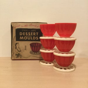 May include: A set of six red plastic dessert molds with white bases. The molds are stacked in a pyramid shape. The box reads "Stack 'n Serve Dessert Plastic Moulds".
