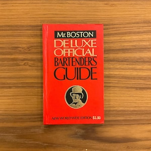 Könnte beinhalten: Ein rotes Buch mit dem Titel Mr. BOSTON DE LUXE OFFICIAL BARTENDER'S GUIDE mit schwarzem Text und einer kreisförmigen Illustration einer Person mit Zylinder. Der Einband enthält unten den schwarzen Text NEW WORLD WIDE EDITION $2.50.