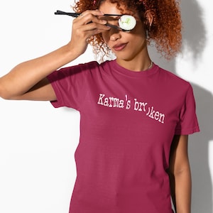 May include: A maroon t-shirt with the text "Karma's broken" in white. The person is holding sushi with chopsticks. The person is wearing a red bandana.