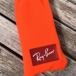 May include: Orange sunglasses case with a red Ray-Ban logo.