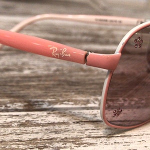 May include: Pink and white Ray-Ban aviator sunglasses with rhinestones on the frame.