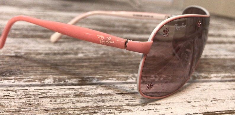 May include: Pink and white Ray-Ban aviator sunglasses with rhinestones on the frame.