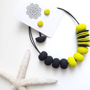 May include: A black and yellow statement necklace with large, chunky beads. The necklace is made of polymer clay and has a modern, geometric design. The necklace comes with a pair of matching earrings.