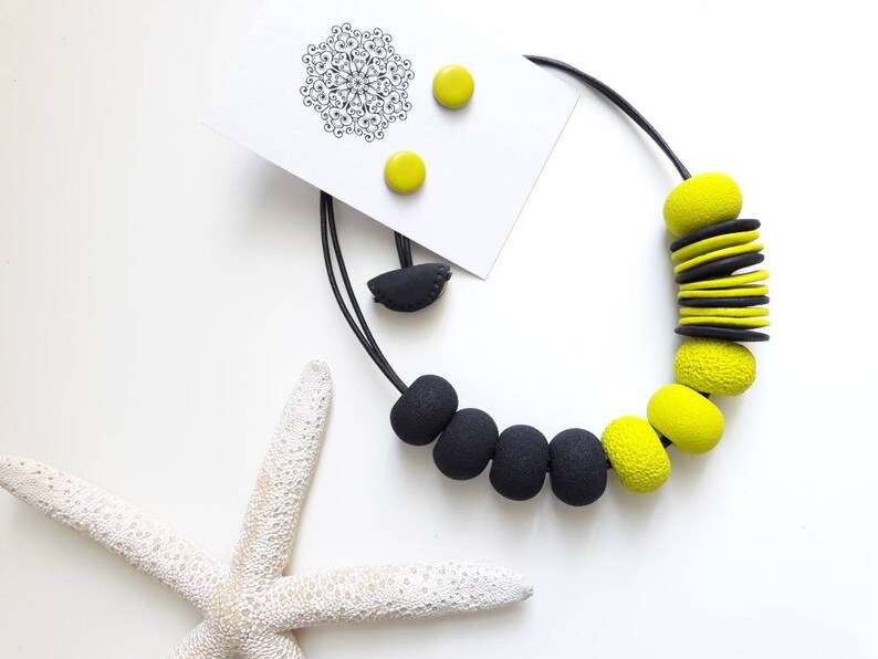 May include: A black and yellow statement necklace with large, chunky beads. The necklace is made of polymer clay and has a modern, geometric design. The necklace comes with a pair of matching earrings.
