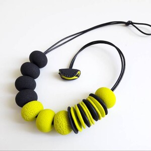May include: A black and yellow statement necklace with large, round beads. The necklace is made of polymer clay and has a simple, modern design.
