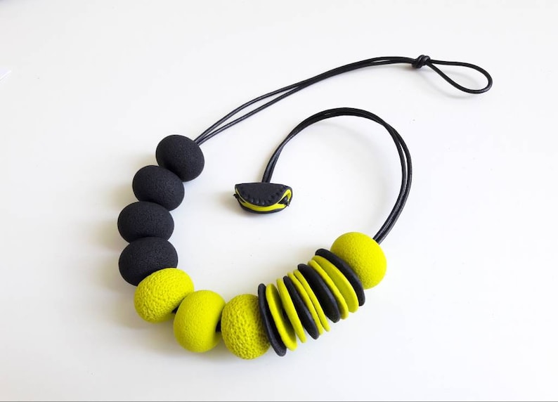 May include: A black and yellow statement necklace with large, round beads. The necklace is made of polymer clay and has a simple, modern design.