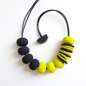 May include: A black and yellow statement necklace with large, round beads and a stack of flat, round beads. The necklace is made of polymer clay.