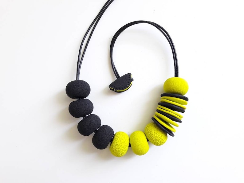 May include: A black and yellow statement necklace with large, round beads and a stack of flat, round beads. The necklace is made of polymer clay.