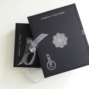 May include: Two black boxes with the text "Dreams. Truly Made." and "justSU" on them. The boxes are tied together with a white ribbon.