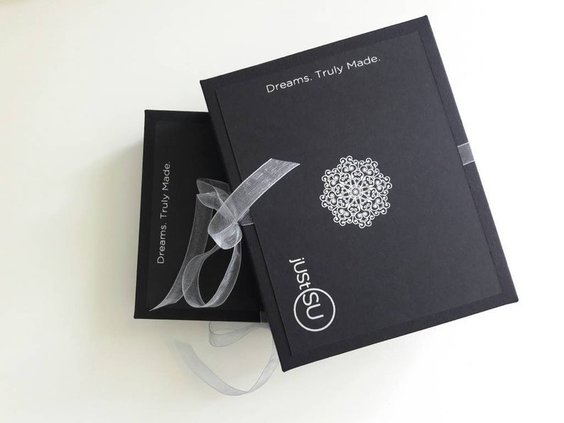 May include: Two black boxes with the text "Dreams. Truly Made." and "justSU" on them. The boxes are tied together with a white ribbon.