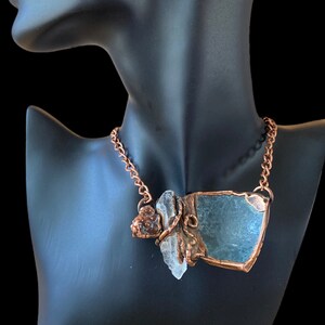 May include: A copper chain necklace with a pendant featuring a large, irregularly shaped, light blue stone, a smaller clear stone, and a copper accent.