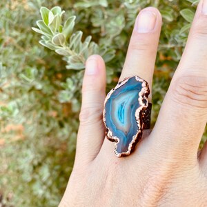 May include: A copper ring with a large, dark blue agate stone set in the center. The agate has a white and blue banded pattern.