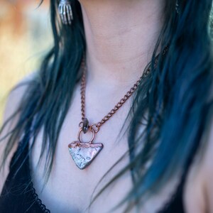 May include: A copper chain necklace with a triangular pendant made of white and brown ceramic. The pendant has a copper ring at the top.