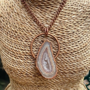 May include: A copper chain necklace with a large, light brown agate pendant. The pendant is set in a copper circle and hangs from a copper chain.