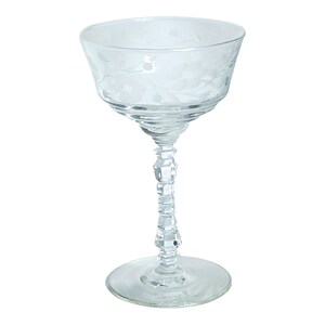 Könnte beinhalten: Ein klares, geätztes Glas mit einer breiten Schale und einem dekorativen Stiel. Das Glas hat ein Blumendesign um den Rand und auf der Schale. Der Stiel hat ein facettiertes Design. Das Glas steht auf einem runden Fuß.