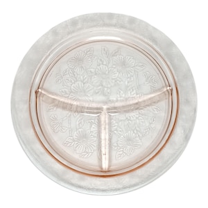 Puede incluir: Un plato de servir transparente, dividido en tres secciones, con un tono rosado. El centro presenta un diseño floral y el borde un patrón texturizado. Ideal para servir aperitivos. Una pieza vintage.