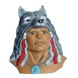 May include: A bust of a Native American man wearing a wolf headdress. The sculpture has a brown complexion, with grey and white fur on the headdress. Red and white accents hang from the sides. A turquoise pendant hangs around the neck.