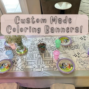 May include: A white tablecloth with a black and white coloring page design featuring a house, palm trees, and the words "Happy Birthday Maci!"  The tablecloth is set with colorful plastic cups and plates.  The text "Custom Made Coloring Banners!" is written in pink on a white background.