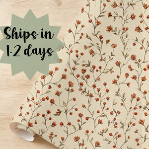 May include: A roll of floral wallpaper featuring a repeating pattern of orange flowers and green leaves on a cream background. The wallpaper is partially unrolled, revealing the pattern. The text "Ships in 1-2 days" is in a green starburst.