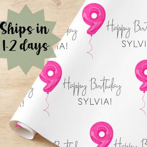 Może przedstawiać: Biały papier do pakowania z powtarzającym się wzorem r&oacute;żowych balon&oacute;w w kształcie cyfry dziewięć i napisem "Happy Birthday SYLVIA!". Papier jest zwinięty w lewym dolnym rogu.