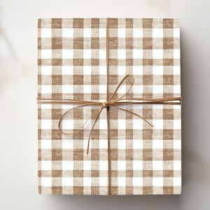 Könnte beinhalten: Ein rechteckiges Geschenk, verpackt in braun-weiß kariertem Papier, mit Bindfaden verschnürt. Der Bindfaden ist zu einer Schleife um das Paket gebunden. Das Geschenkpapier hat ein Vichy-Muster.