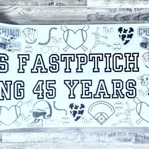 May include: A white banner with black text and graphics celebrating 45 years of Girls Fastpitch. The banner features a baseball diamond, bats, hearts, and cow graphics. The text on the banner reads "Girls Fastpitch Celebrating 45 Years".