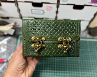 May include: A rectangular green leather box featuring an embossed dragon scale pattern across the surface. The box is secured with two antique brass-colored metal swing latches on the front flap, which is stitched along the edges.