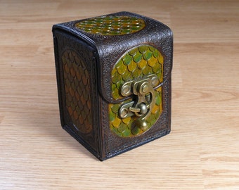 May include: A small, brown leather box with a green and gold scale pattern. The box has a brass latch and is closed.