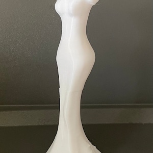 May include: White plastic mannequin torso with a long, flowing skirt. The mannequin is standing on a dark surface.