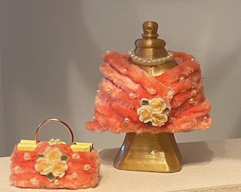 May include: A miniature peach-colored purse with a gold handle and a matching shawl on a gold mannequin. Both items are adorned with pearls and floral accents, creating a vintage aesthetic. The purse is approximately 3 inches wide.