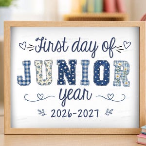 May include: A framed sign with the text First day of JUNIOR year 2026-2027. The word JUNIOR features blue and white patterns including gingham, floral, stars, and polka dots. The text is accented with small hearts and leaf flourishes in dark blue.