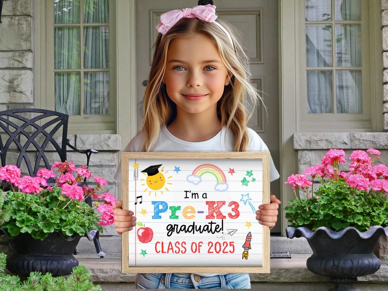 K&ouml;nnte beinhalten: Ein M&auml;dchen h&auml;lt ein Schild mit der Aufschrift "Ich bin ein Pre-K3 Absolvent! Klasse von 2023". Das Schild ist mit einem Regenbogen, Sternen, einer Rakete und einer Sonne mit einem Abschluss-Hut verziert.