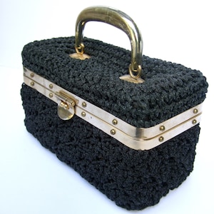 May include: A black crocheted handbag with a gold metal handle and clasp. The bag has a rectangular shape and a textured surface.