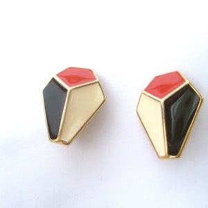 May include: A pair of geometric shaped earrings with a gold finish. The earrings are red, black, and white.