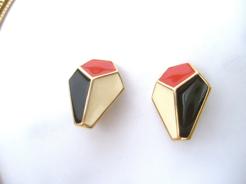 May include: A pair of geometric shaped earrings with a gold finish. The earrings are red, black, and white.