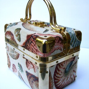 K&ouml;nnte beinhalten: Eine vintage, rechteckige Handtasche aus Stoff mit goldfarbenem Metallrahmen und Griff. Der Stoff hat ein farbenfrohes Muschelmuster.