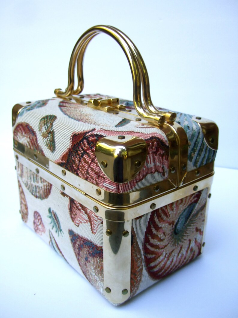 K&ouml;nnte beinhalten: Eine vintage, rechteckige Handtasche aus Stoff mit goldfarbenem Metallrahmen und Griff. Der Stoff hat ein farbenfrohes Muschelmuster.