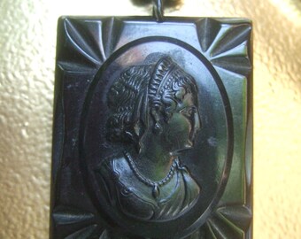 May include: A black jet necklace with a cameo pendant featuring a woman's profile in relief. The cameo is set in a square frame with a decorative design.