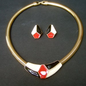 May include: A gold chain necklace with a black, white, and red geometric pendant. Matching earrings with the same geometric design.