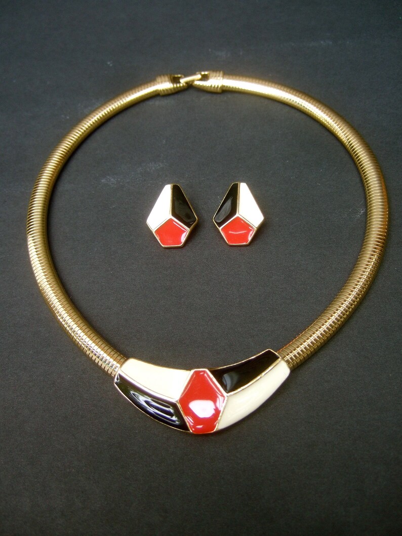 May include: A gold chain necklace with a black, white, and red geometric pendant. Matching earrings with the same geometric design.