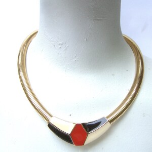 May include: A gold chain necklace with a geometric pendant featuring black, white, and red enamel.