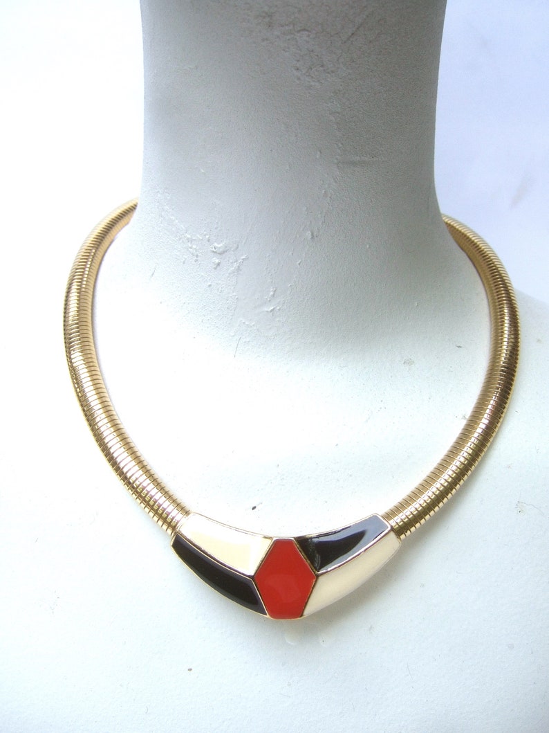 May include: A gold chain necklace with a geometric pendant featuring black, white, and red enamel.