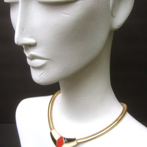 May include: A gold chain necklace with a geometric pendant featuring red, black, and white enamel.