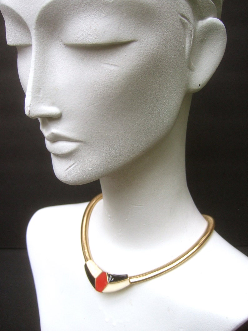 May include: A gold chain necklace with a geometric pendant featuring red, black, and white enamel.
