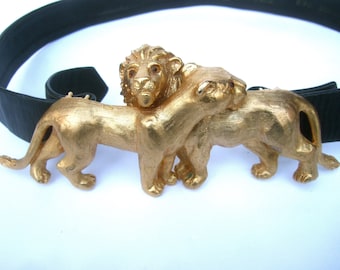 Könnte beinhalten: Eine goldfarbene Gürtelschnalle mit zwei Löwen, einer mit dem Kopf zur Seite gedreht und der andere mit dem Kopf nach vorne gerichtet. Die Löwen sind aufwendig detailliert und haben eine strukturierte Oberfläche.