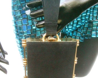 May include: A black velvet evening bag with a gold frame and a black leather strap. The bag has a rectangular shape and a clasp closure.