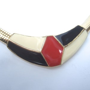 May include: A gold chain necklace with a geometric pendant featuring black, white, and red enamel.