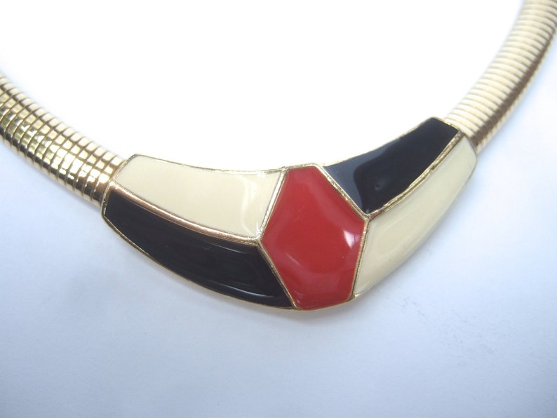 May include: A gold chain necklace with a geometric pendant featuring black, white, and red enamel.